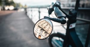 Best Bike Mirrors: A reflection of a building from a bike mirror attached to a bike on a street near river