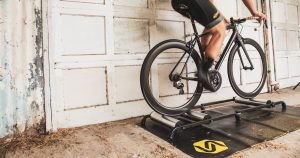 Best Bike Rollers: A cyclists riding on Saris bike rollers in front of a garage door