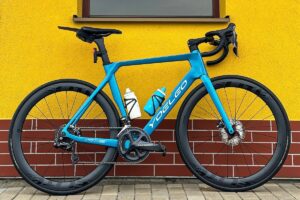 My blue YOELEO R12 Chinese carbon road bike with Elitewheels ENT wheels Chinese carbon wheels in front of a yellow bus station with a square window.
