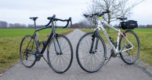 Road bike vs. hybrid bike: Road bike on the left side and a hybrid bike on the right side (side-by-side) on a bicycle path.