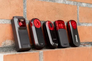 What is a bicycle radar and how does it work: Multiple cycling radars in a row (Tutuloo W100, Garmin Varia RTL515, Magene L508, Bryton Gardia R300L, iGPSport SR30) stacked side by side on a brick wall.